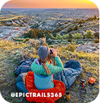 Woman sitting outside looking through binoculars at a valley and sunset below her, with overlay text that reads: @epictrails365