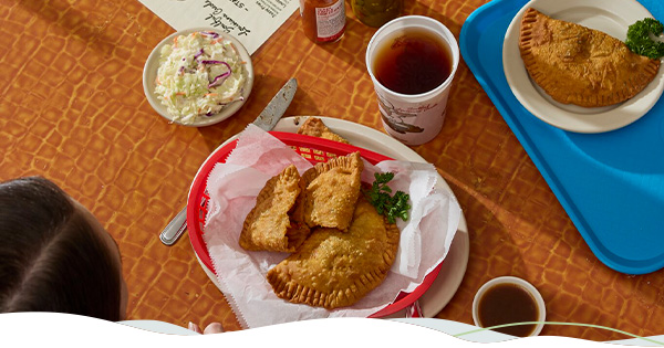 A table filled with meat pies and all the fix-ins, including coleslaw and sauces.