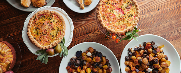 Looking down at a table with prepared dishes such as potatoes, quiches and chicken. 