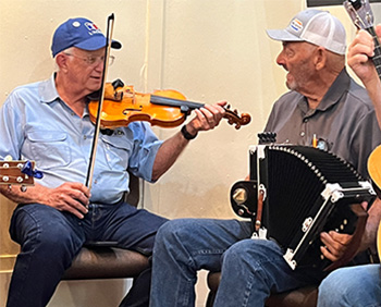 Two older men playing Cajun music with a fiddle and accordion.