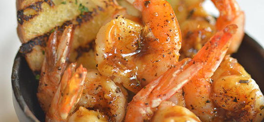 Bowl of grilled shrimp served with bread on the side.