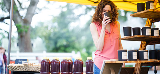 Woman smelling a candle at an outdoor market stand.