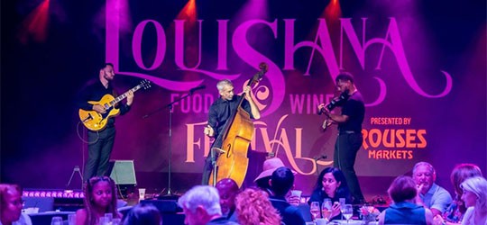 A band performing on stage, with a background displaying Louisiana's Food & Wine Festival.
