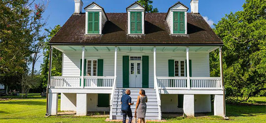 A couple walks towards the main building at the E.D. White Historic Site, a white-paneled house with bright green shutters.