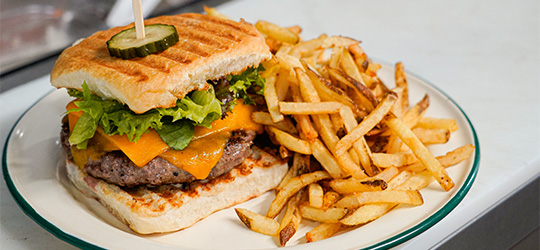 A grilled cheddar cheeseburger with lettuce and pickles is served on toasted bread with a side of fries.