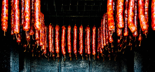 Dozens of smoked sausages hang in rows inside a black smoker.