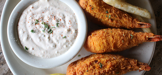 A plate holds fried shrimp, fries, and a bowl of creamy dipping sauce.