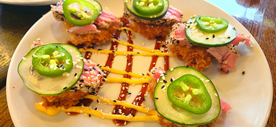Spicy tuna bites are topped with jalapeño slices and drizzled with sauces on a white plate.