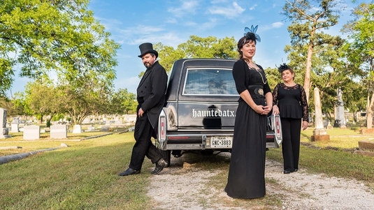 Three tour guides dressed in black from Haunted ATX Hearse Limousine stand next to a hearse in Austin, Texas