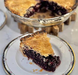 slice of blueberry pie on a plate in front of the full pie 