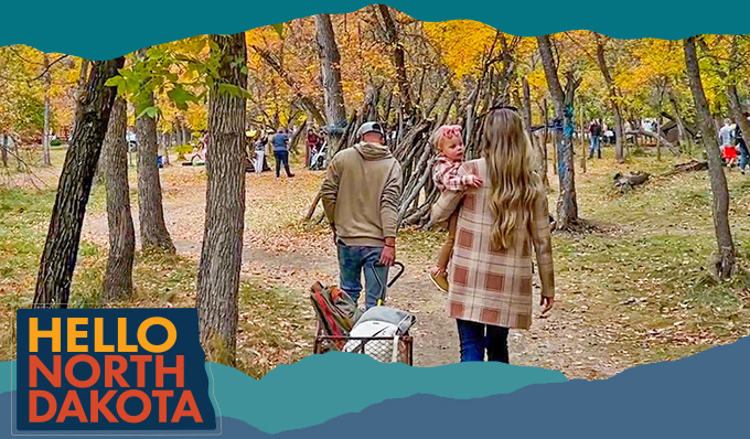View from behind of a man, woman and child walking a path through trees with orange leaves, with overlay text that reads: Hello North Dakota