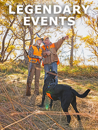 Woman and a man wearing orange and brown hunting outfits, standing in a wooded area with a black dog and pointing into the distance, with overlay text that reads: Legendary Events