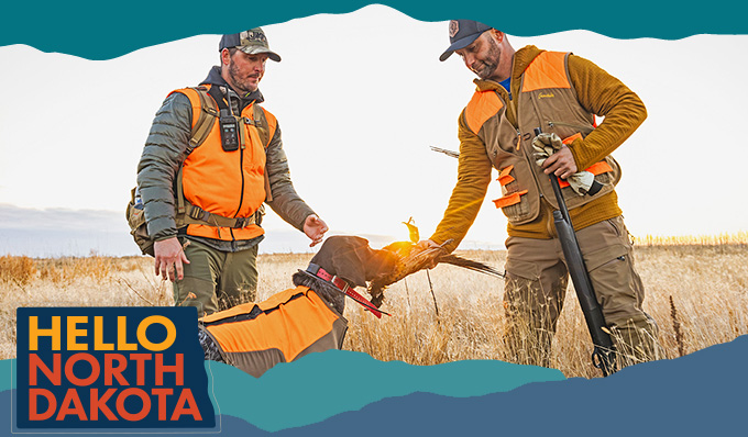 Two men wearing orange and brown hunting outfits with a dog holding a dead bird in a field, with overlay text that reads: Hello North Dakota