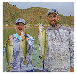 A woman and a man standing on a boat holding caught fish, with a rock formation behind them