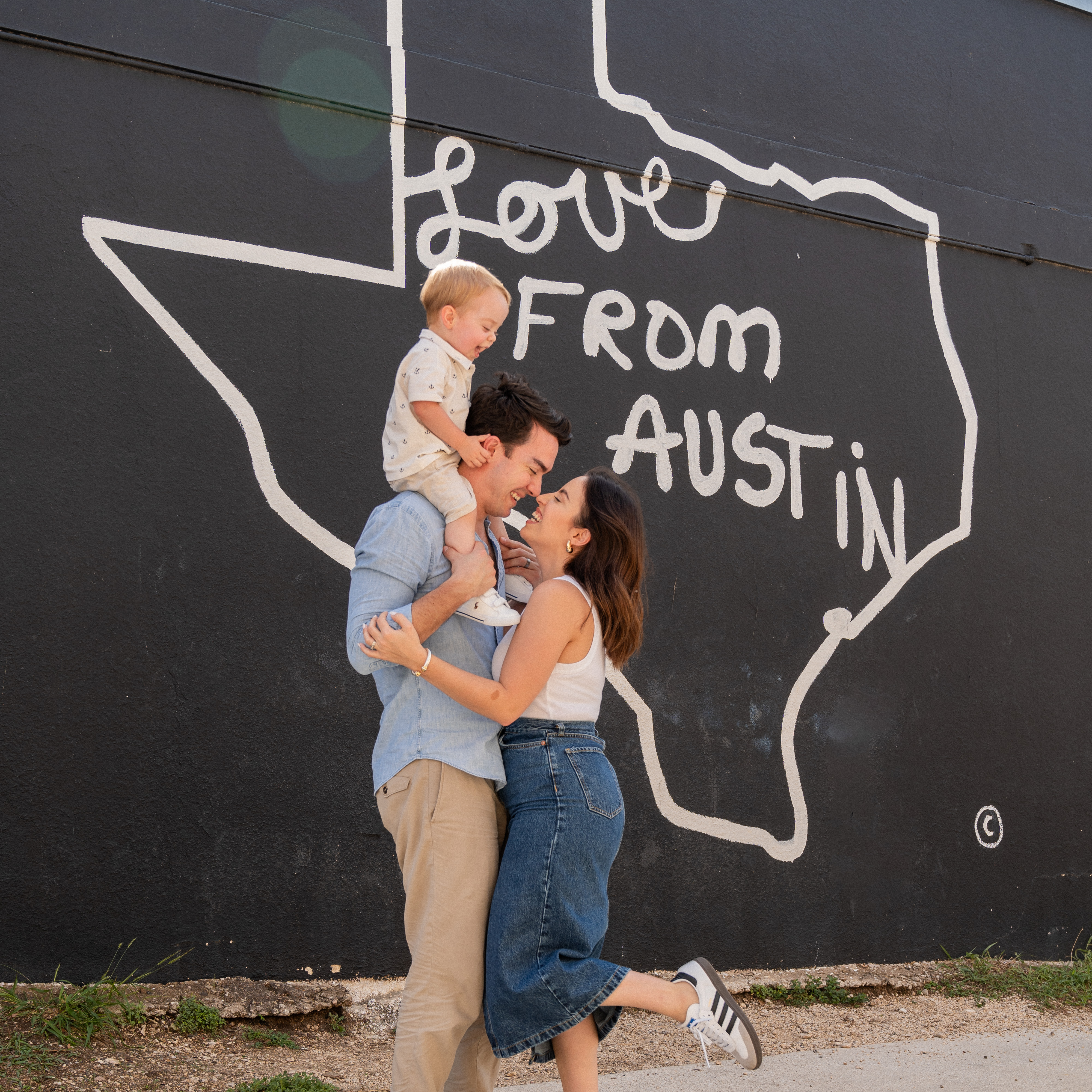 A man, woman and child in front of a mural featuring the outline of Texas and the words Love from Austin