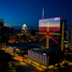 Exterior view of the Fairmont Austin at night with red and gold lights forming a bow shape on the building