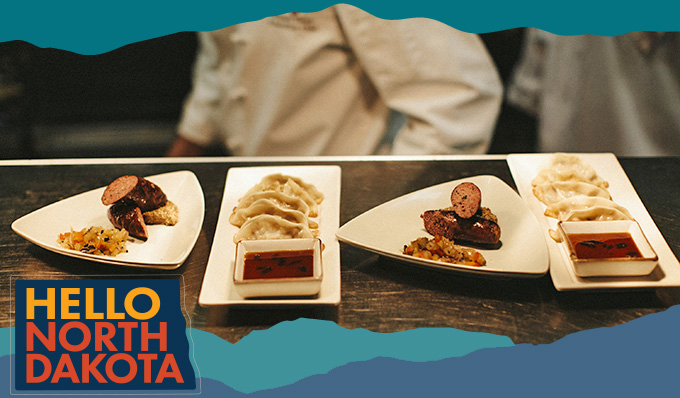 Wood table at a restaurant with dishes like sausage and potstickers on white plates, with overlay text that reads: HELLO NORTH DAKOTA
