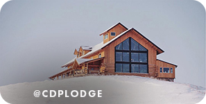 Wood lodge with large windows on top of a snowy hill, with overlay text that reads: @cdplodge