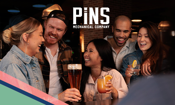 Two men and three women holding beverages smile and pose inside Pins Mechanical Co. in Austin, Texas