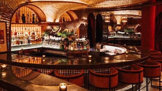 A curved marble bar with velvet barstools, dim candlelight, mirrored walls and arched shelves inside the Powder Room in Austin, Texas