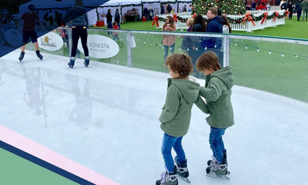 Two children hold on to each other while ice skating outdoors at the Hill Country Galleria