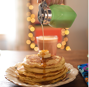 Maple syrup being poured over a stack of pancakes