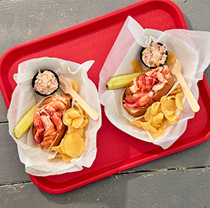 Red tray with two lobster rolls, chips and pickles