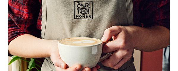 Barista serving a warm latte at Cafe Nomad