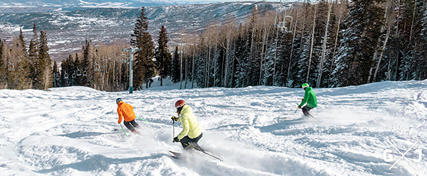 Three skiers in bright puffers schuss down a mountainside with plenty of snow at Powderhorn Mountain Resort near Grand Junction, Colorado.