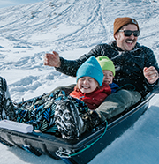 An adult and two kids flash big smiles after sledding down a snowy hill near Grand Junction, Colorado.