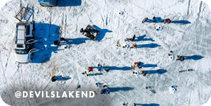 Aerial view of people ice fishing on a frozen lake, with overlay text that reads: @devilslakend