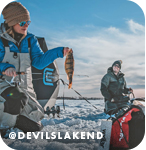 Two people ice fishing on a snowy frozen lake, with overlay text that reads: @devilslakend