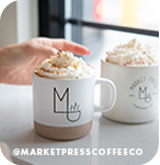 Hand reaching for two mugs of coffee beverages topped with whipped cream, with overlay text that reads: @marketpresscoffeeco