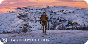 View from behind of a person walking on snowy ground with snowy mountains and a pink sky ahead of them, with overlay text that reads: @beagleboyoutdoors