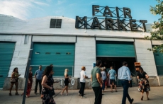 People walk toward an open garage-style door at Fair Market, an indoor-outdoor event space in East Austin