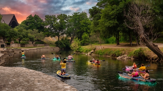 A group of people kayak and paddleboard on the Comal River in New Braunfels, Texas