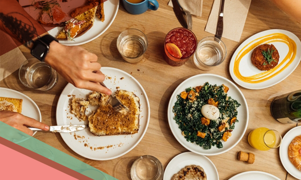 A person's hands use a knife and fork to cut French toast on a table filled with brunch dishes at Paperboy on South Lamar in Austin
