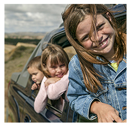 Two young girls and a boy leaning out the windows of a car