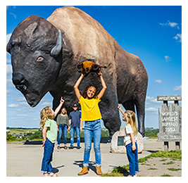 A family of three young girls and parents posing in front of a large statue of a bison