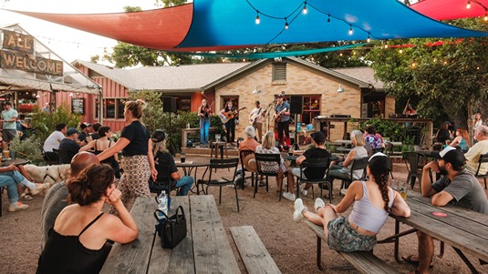 A band performs on an outdoor stage as people sit at picnic tables at Radio Coffee & Beer in Austin 