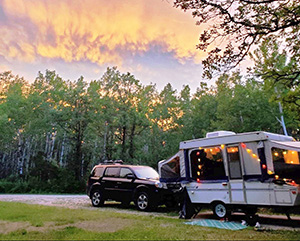 Car and a camper at a site surrounded by trees and sunset