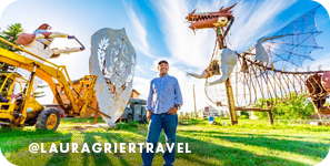 Man standing in front of metal sculptures of a dragon, tractor and more, with overlay text that reads: @lauragriertravel