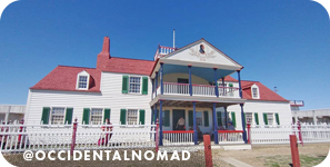Large white farm-style house with green shutters, red roof and a balcony, with overlay text that reads: @occidentalnomad