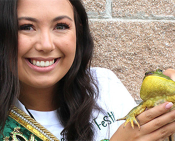 A woman smiles, holding up a bright green frog.