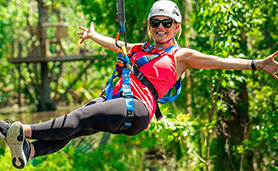 A woman smiles on a zip-line in a lush, green forest.