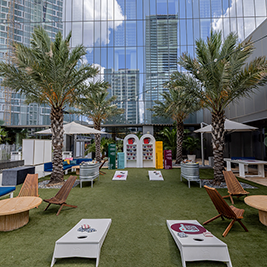 Outdoor recreation area with artificial turf, tables, chairs and cornhole games on the rooftop of Fairmont Austin, surrounded by the Austin, Texas, skyline