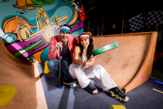 Two people dressed in colorful, retro-style clothing sit on a wooden ramp painted with graffiti inside Holey Moley in Austin