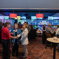 People sit, stand and mingle with bowling lanes and large screens behind them inside the PINSTACK venue in Austin, Texas