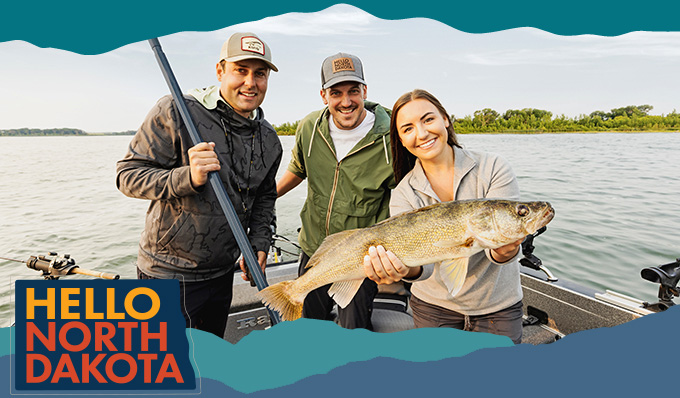 Two men and a woman on a fishing boat holding a large fish with water in the background, with overlay text that reads: Hello North Dakota