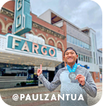 A man smiling and posing in front of an Art Deco building with a neon sign that says Fargo, with overlay text that reads: @paulzantua